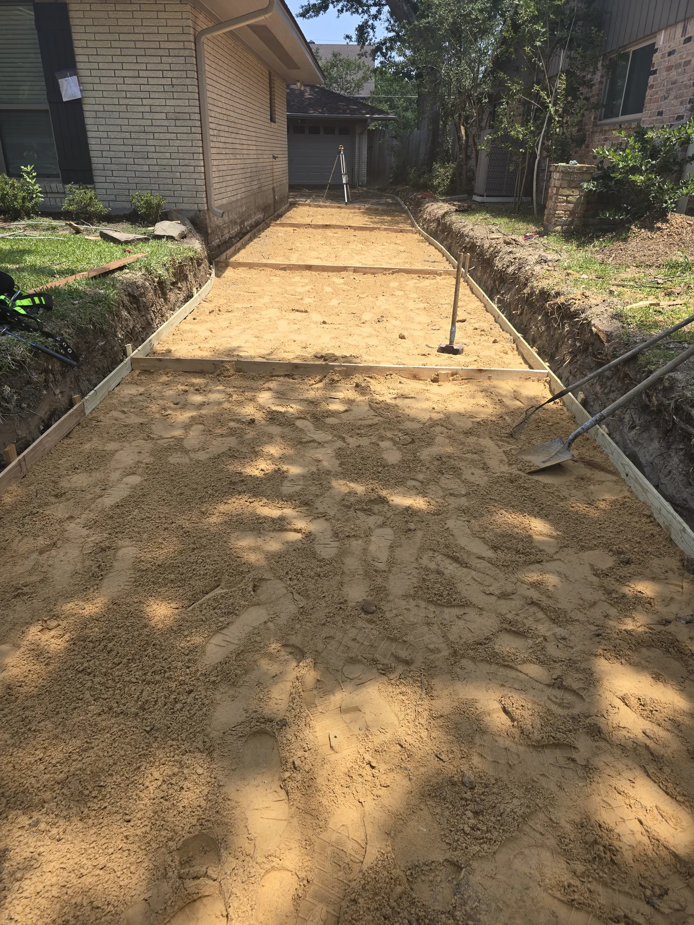 Driveway base and formwork beside a brick home before the pour, photographed May 2025