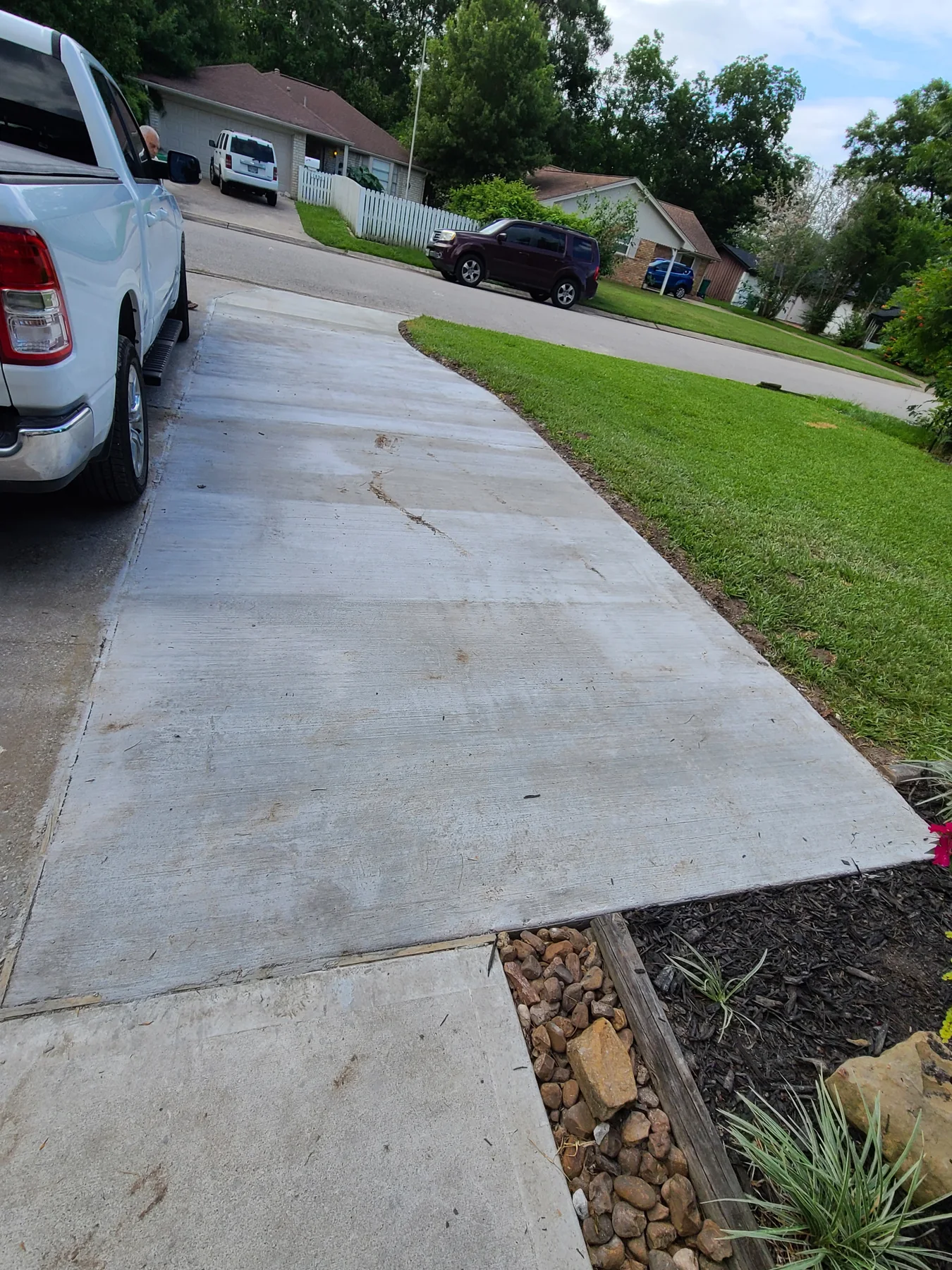 Concrete driveway extension with a curved lawn edge beside existing concrete, photographed June 2024