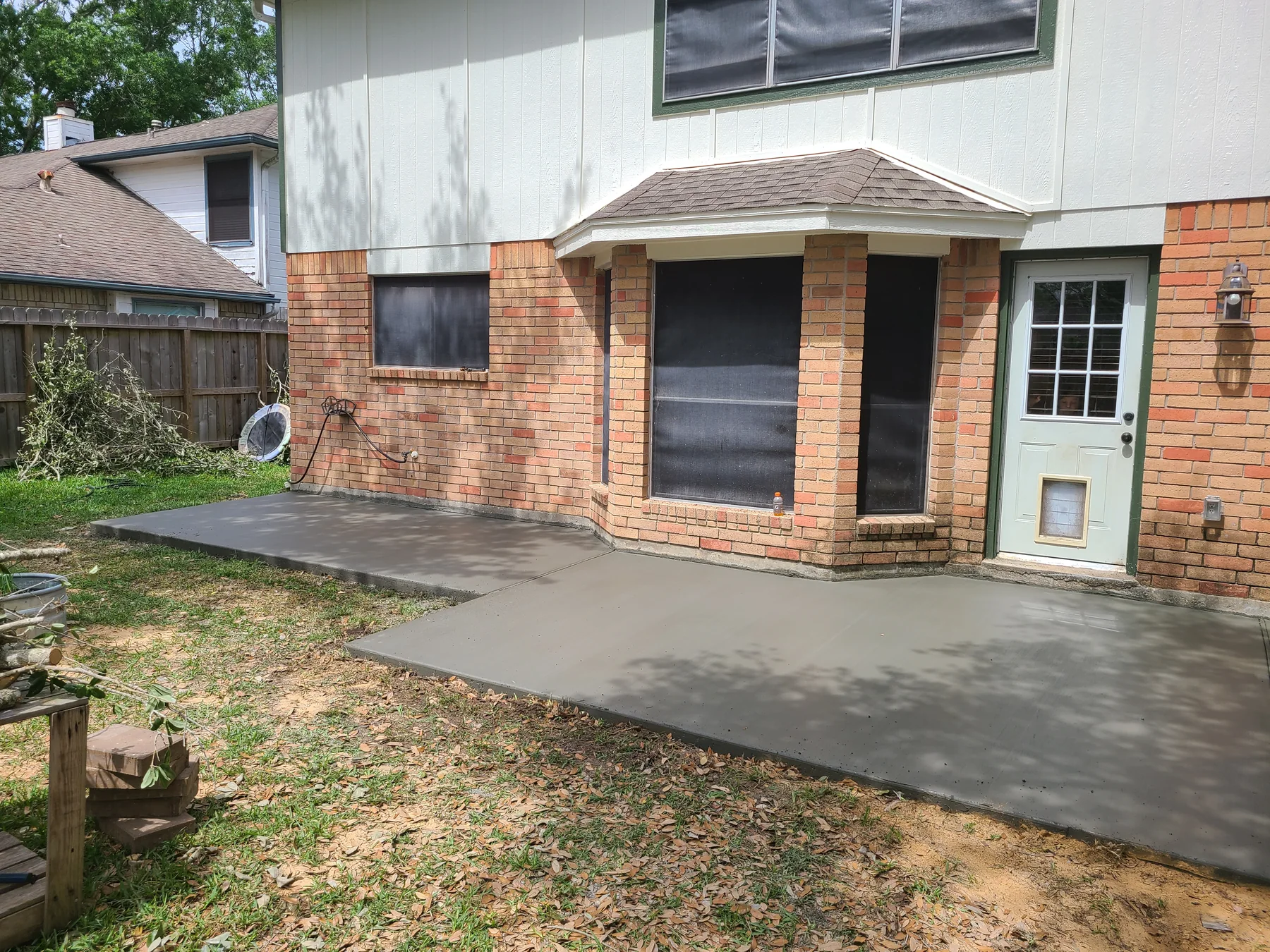 Fresh concrete backyard patio wrapping around a brick home, photographed April 2023